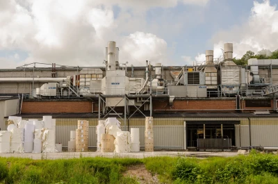 Fabrik technischen Anlagen und Schloten. Im Vordergrund lagern große Berge mit industriellen Papierrollen.