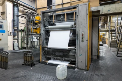 große industrielle Druckmaschine mit einer breiten Papierbahn am Anleger in einer Fabrikhalle